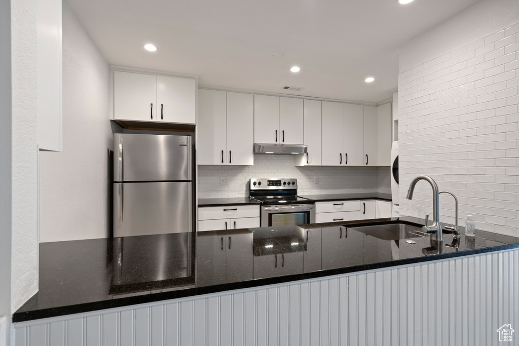 Kitchen featuring dark stone counters, white cabinetry, appliances with stainless steel finishes, backsplash, and sink