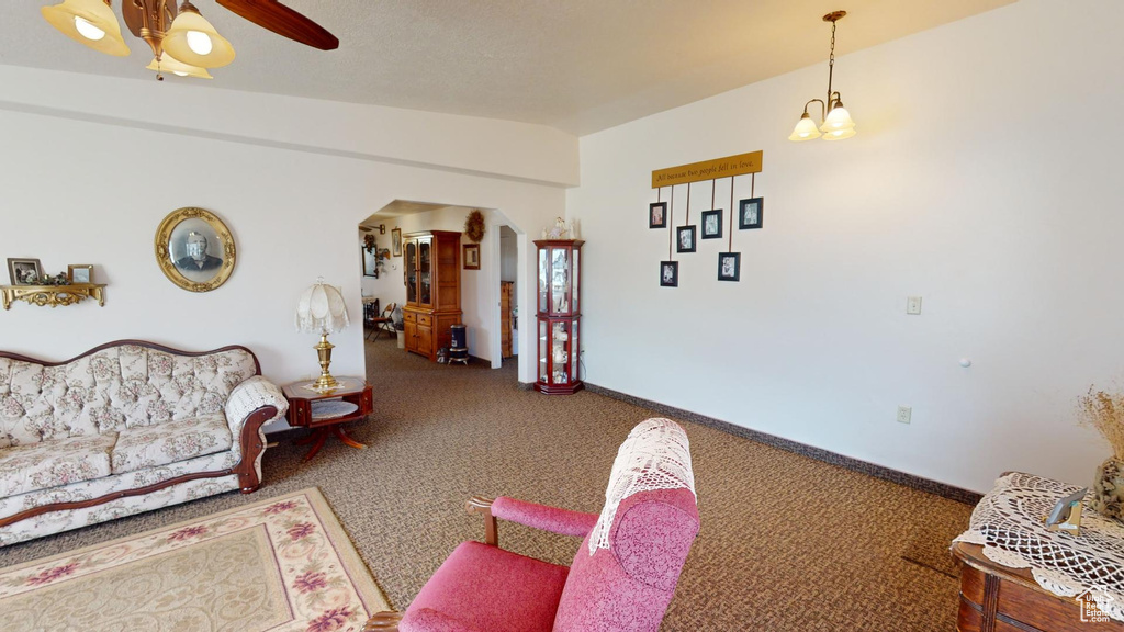 Living room with dark carpet, vaulted ceiling, and ceiling fan with notable chandelier