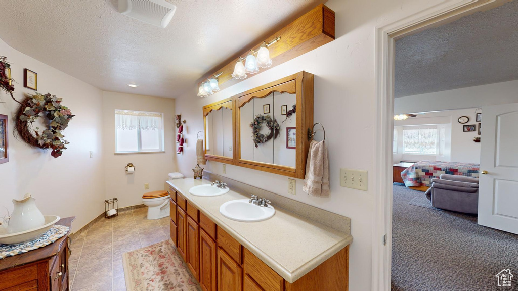 Bathroom with toilet, a textured ceiling, tile floors, and dual vanity