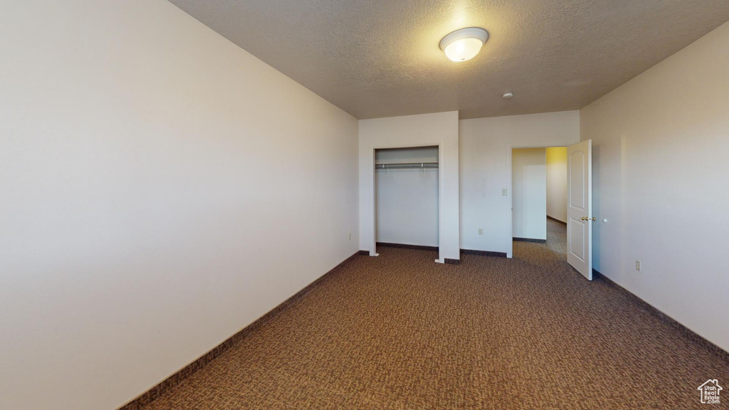 Unfurnished bedroom with a closet, a textured ceiling, and dark colored carpet