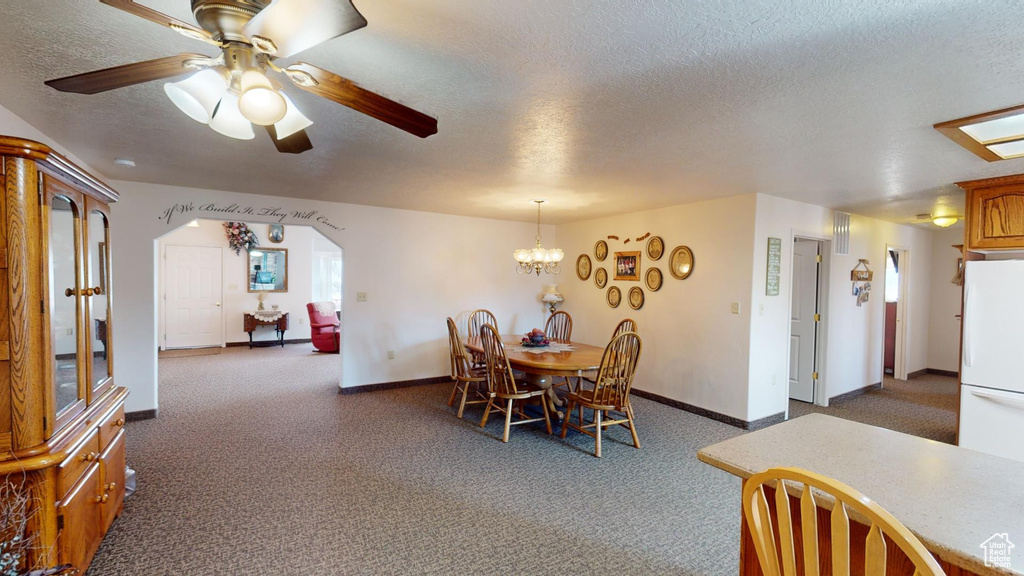 Dining space with a textured ceiling, ceiling fan with notable chandelier, and dark colored carpet