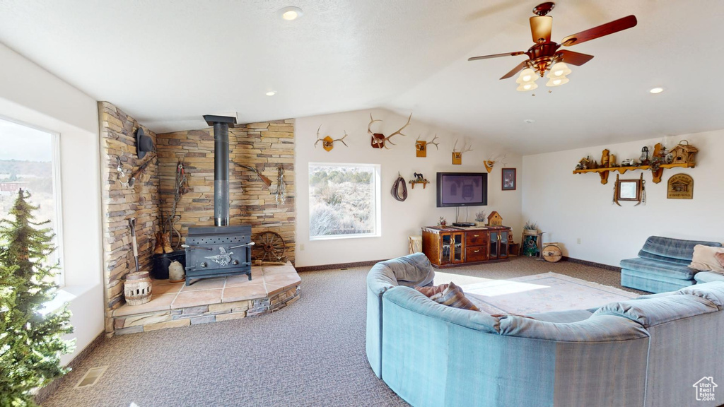 Living room with lofted ceiling, ceiling fan, a wood stove, and light colored carpet