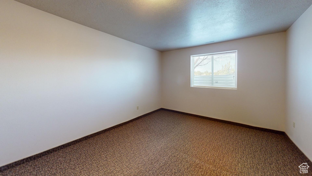 Empty room with a textured ceiling and dark colored carpet