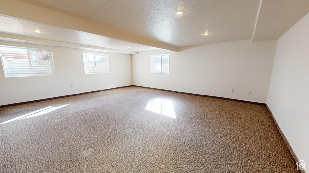 Empty room with carpet, a textured ceiling, and beam ceiling