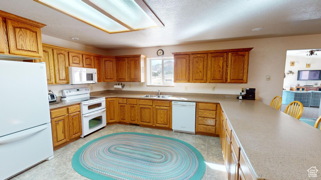 Kitchen featuring light tile flooring, a textured ceiling, a breakfast bar, white appliances, and sink