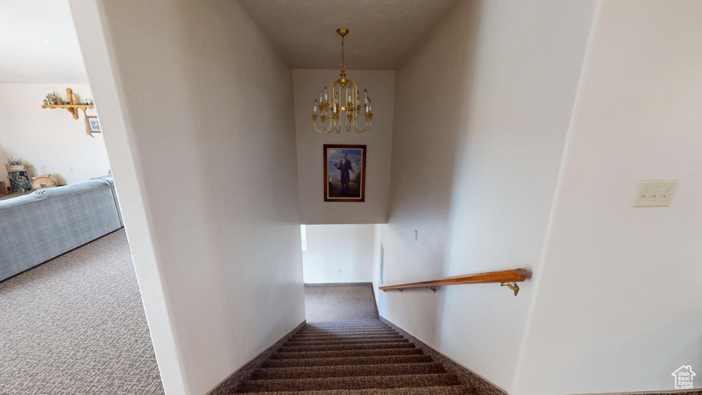 Staircase featuring an inviting chandelier and dark colored carpet