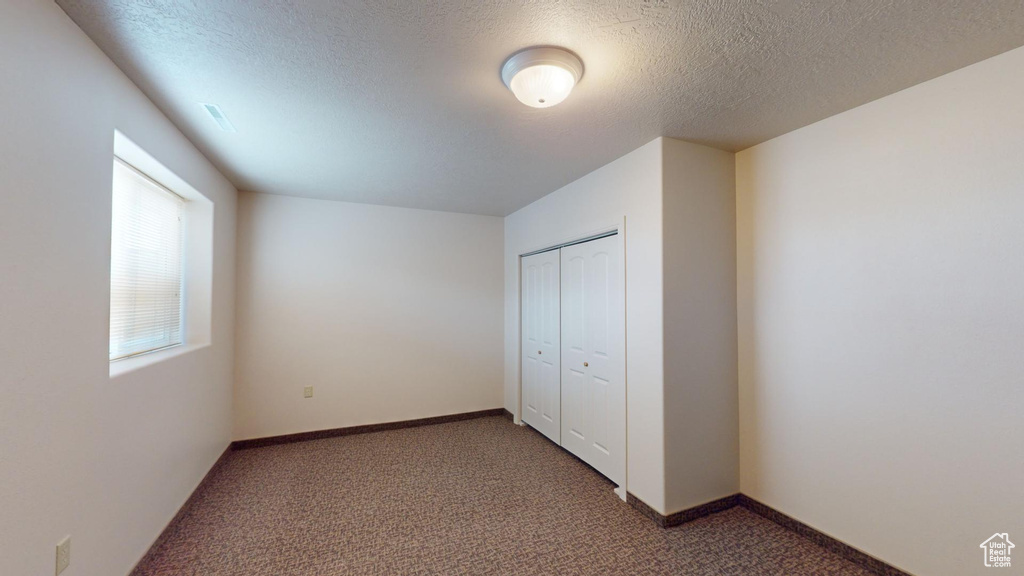 Unfurnished bedroom featuring a textured ceiling, a closet, and dark carpet