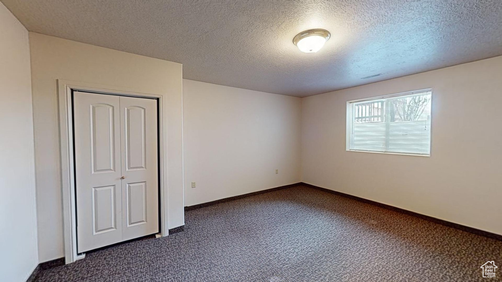 Unfurnished bedroom with a closet, a textured ceiling, and dark colored carpet