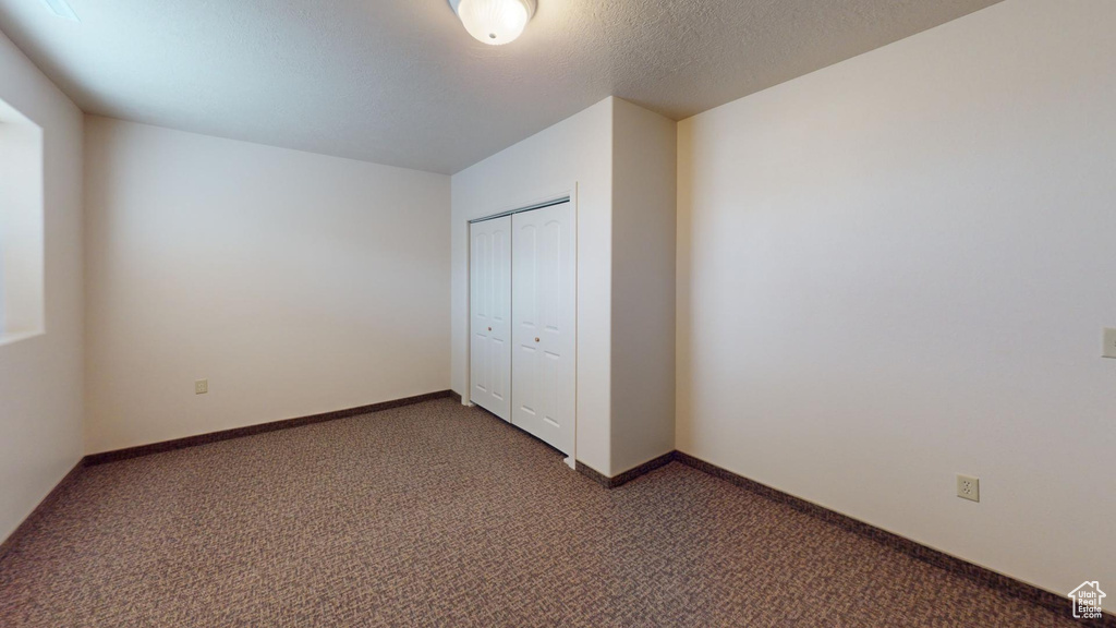 Unfurnished bedroom featuring a textured ceiling, a closet, and dark colored carpet