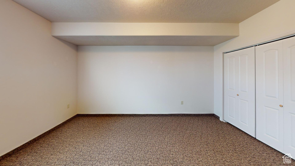 Unfurnished bedroom featuring a closet, a textured ceiling, and dark colored carpet