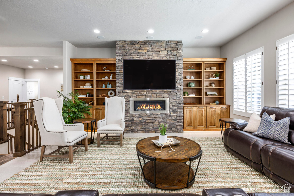 Living room with built in features, a textured ceiling, a stone fireplace, and light tile floors