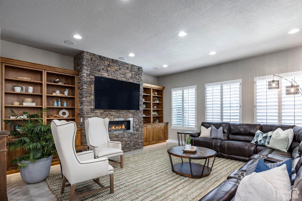 Living room with built in shelves, a stone fireplace, and a textured ceiling