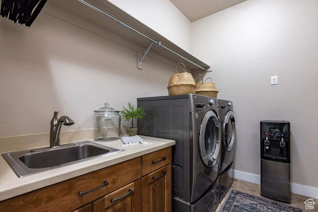 Clothes washing area featuring washer and clothes dryer, sink, and light tile floors