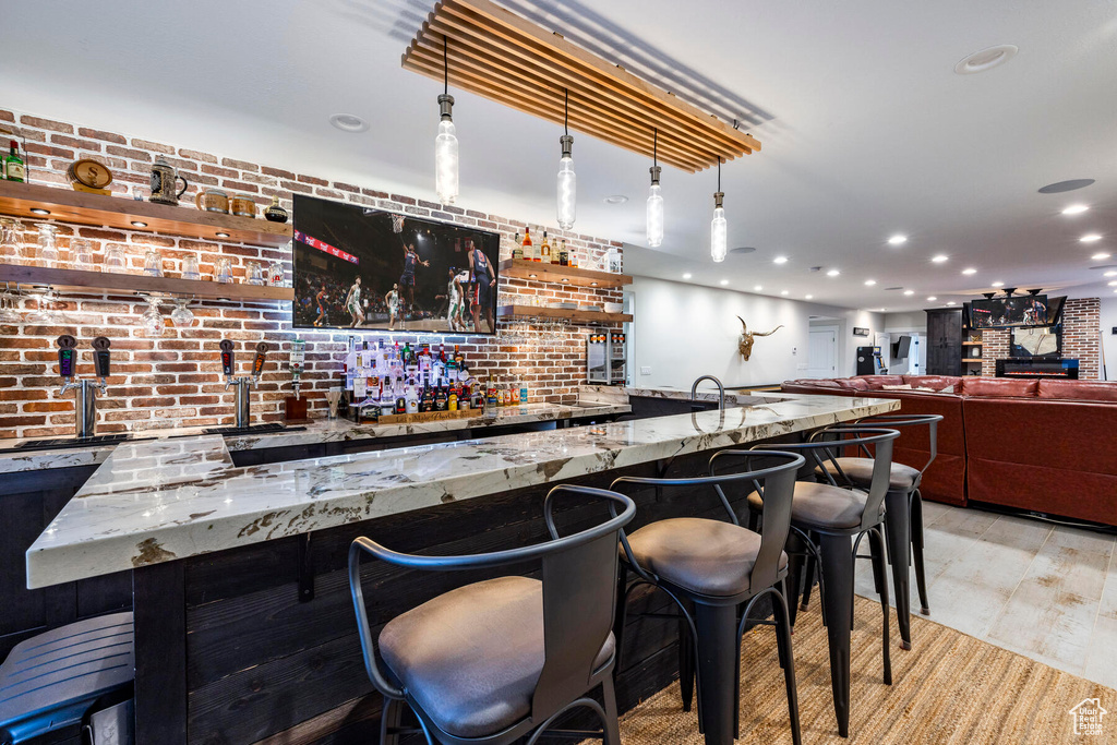 Bar featuring hanging light fixtures, light stone countertops, and light hardwood / wood-style flooring