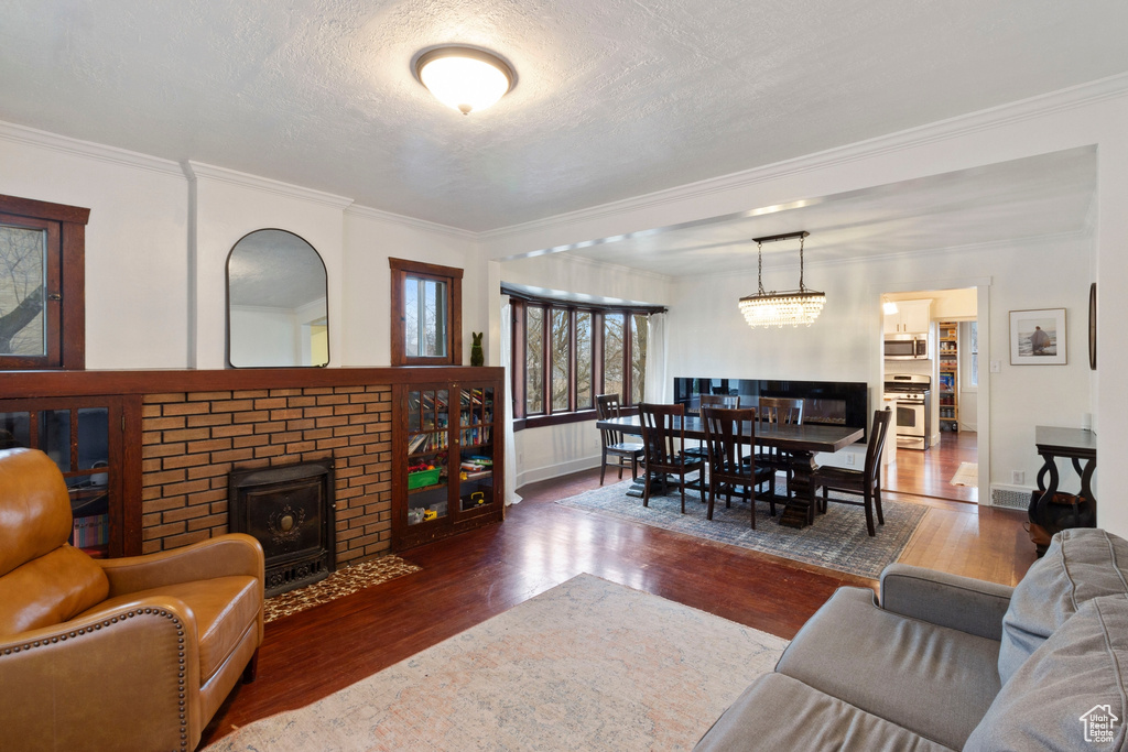 Living room with dark wood-type flooring, a brick fireplace, a textured ceiling, a chandelier, and ornamental molding