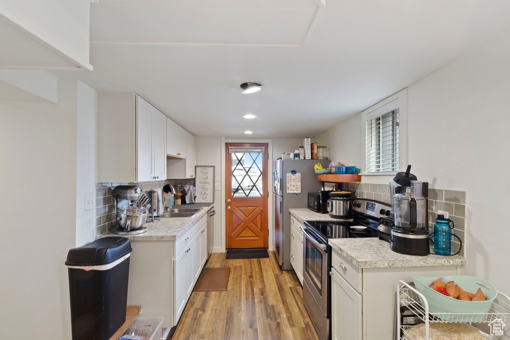 Kitchen featuring backsplash, sink, light wood-type flooring, white cabinets, and stainless steel electric stove