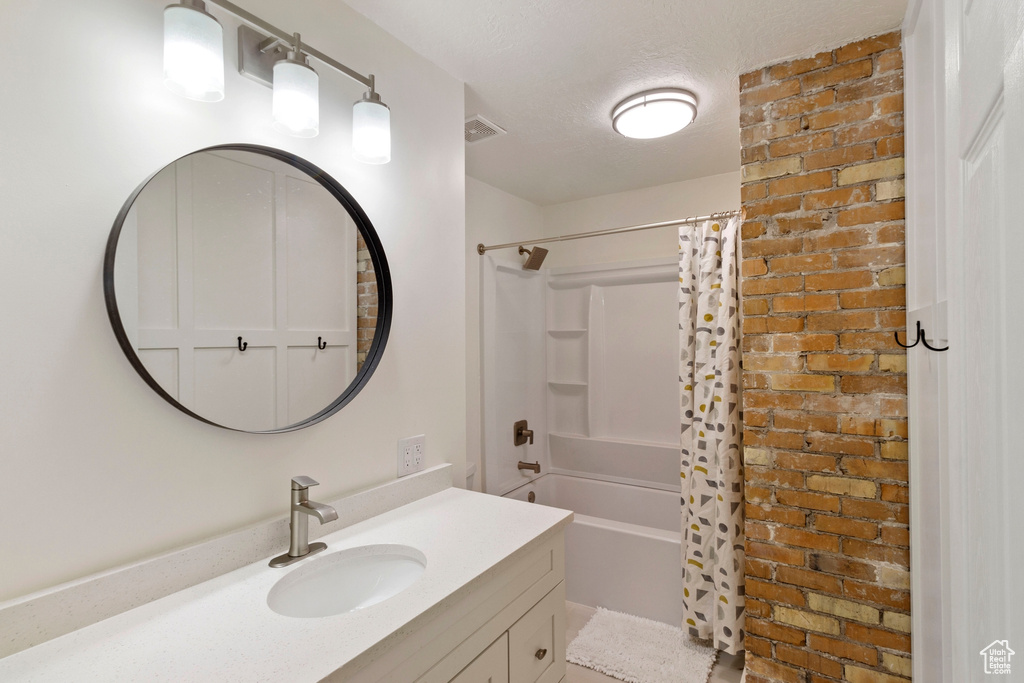 Bathroom with vanity, a textured ceiling, shower / tub combo with curtain, and brick wall