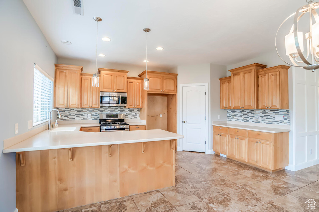 Kitchen featuring tasteful backsplash, appliances with stainless steel finishes, hanging light fixtures, and sink