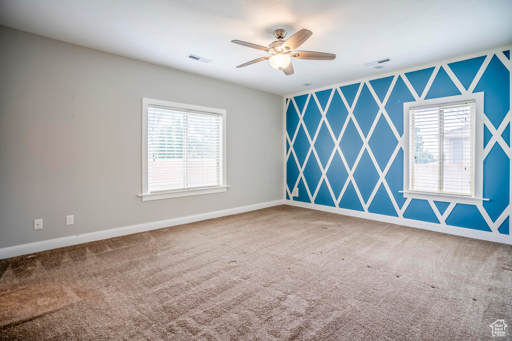 Unfurnished room featuring ceiling fan, carpet, and a wealth of natural light