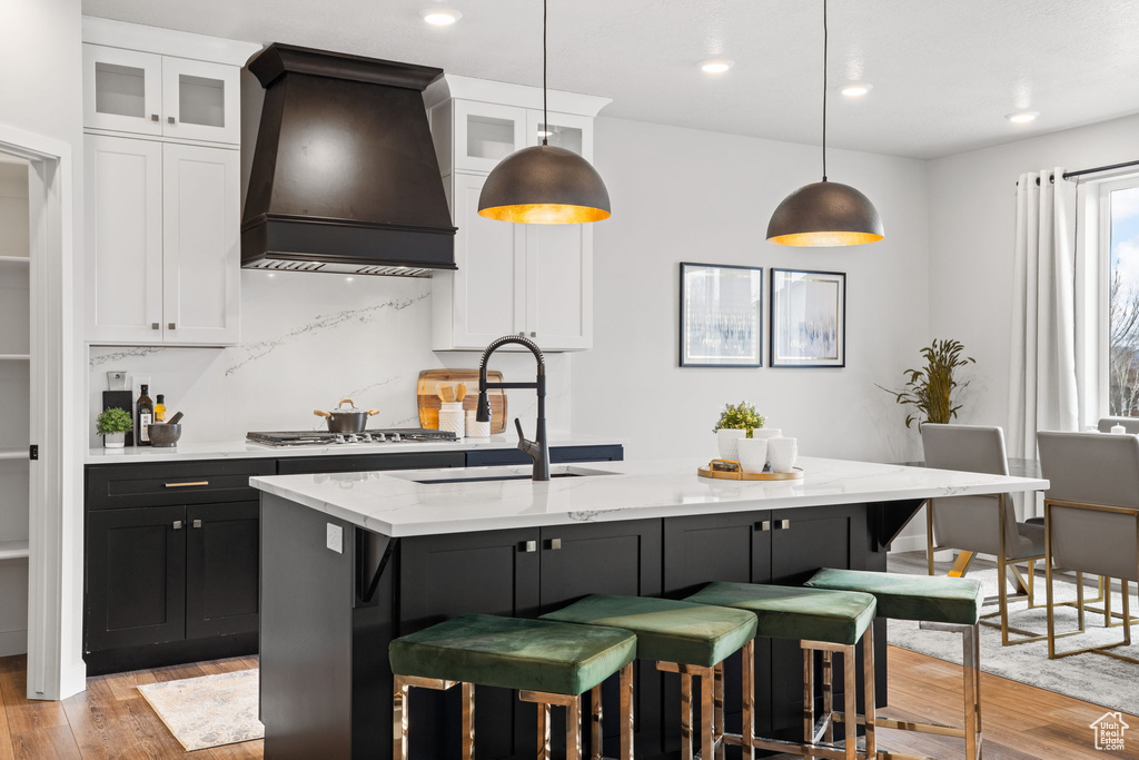 Kitchen with light hardwood / wood-style flooring, a kitchen breakfast bar, decorative light fixtures, and custom exhaust hood