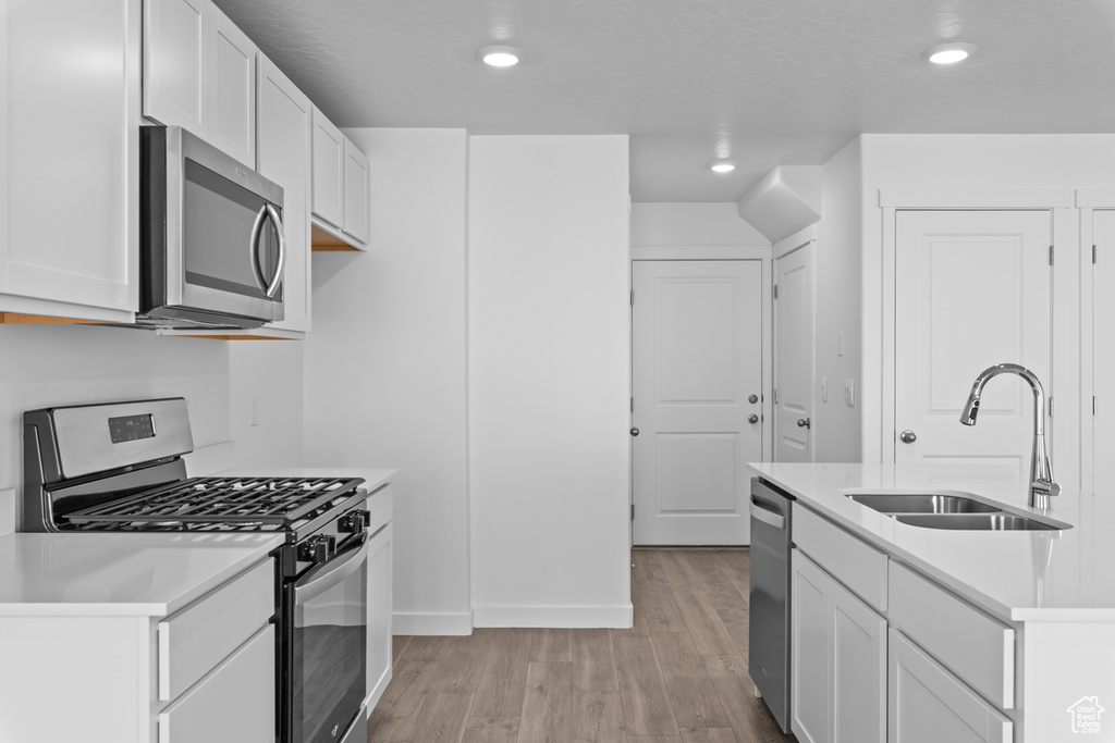 Kitchen featuring white cabinets, appliances with stainless steel finishes, sink, and light hardwood / wood-style flooring