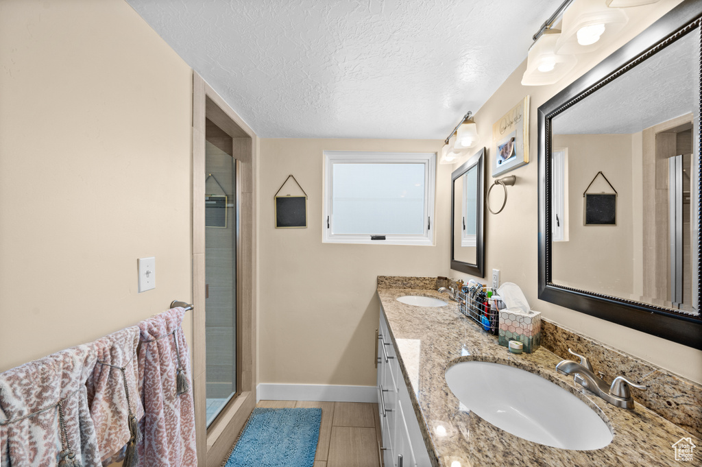 Bathroom with double sink vanity, a textured ceiling, tile floors, and a shower with shower door