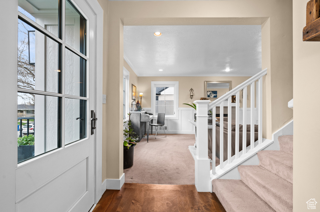 Foyer entrance with ornamental molding, a healthy amount of sunlight, and dark colored carpet