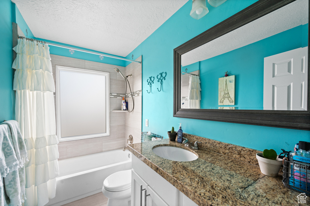 Full bathroom featuring shower / tub combo, a textured ceiling, toilet, and vanity