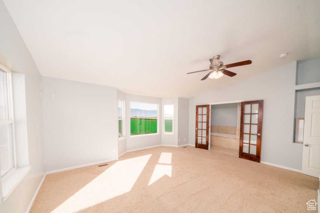 Carpeted spare room featuring lofted ceiling, ceiling fan, and french doors