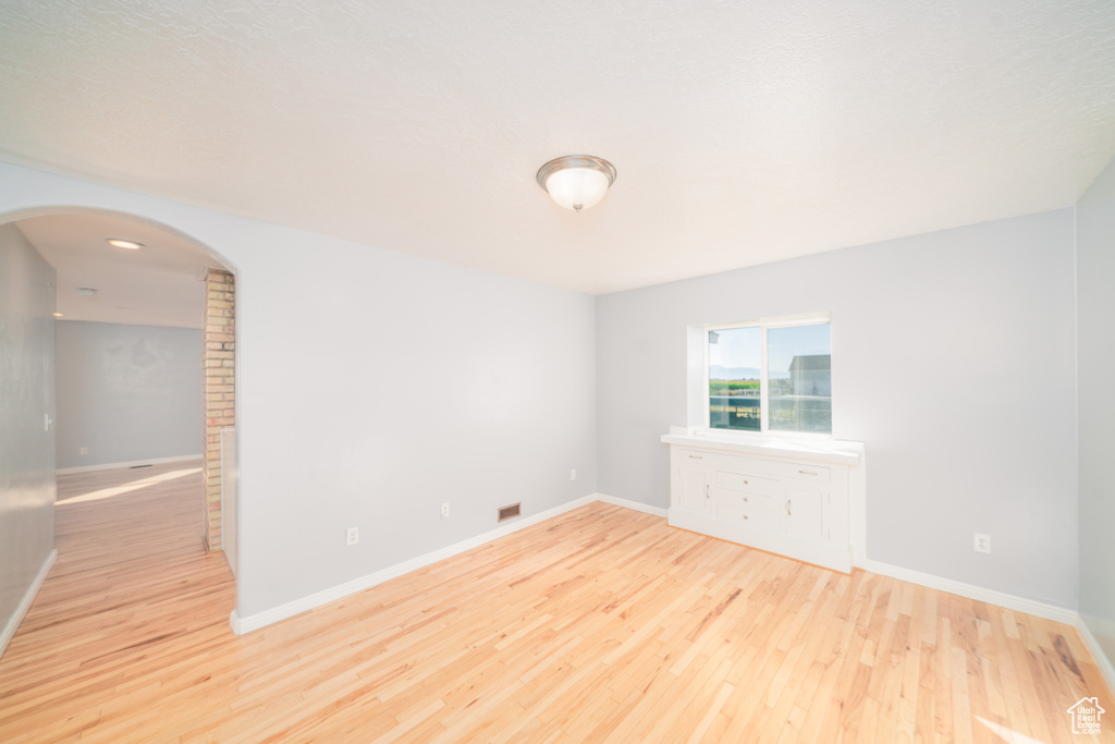 Empty room with brick wall and light hardwood / wood-style floors
