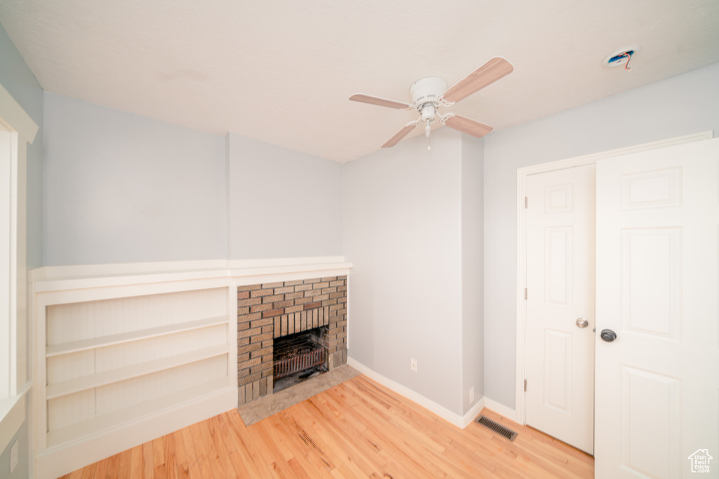 Unfurnished living room featuring ceiling fan, a brick fireplace, and light hardwood / wood-style flooring