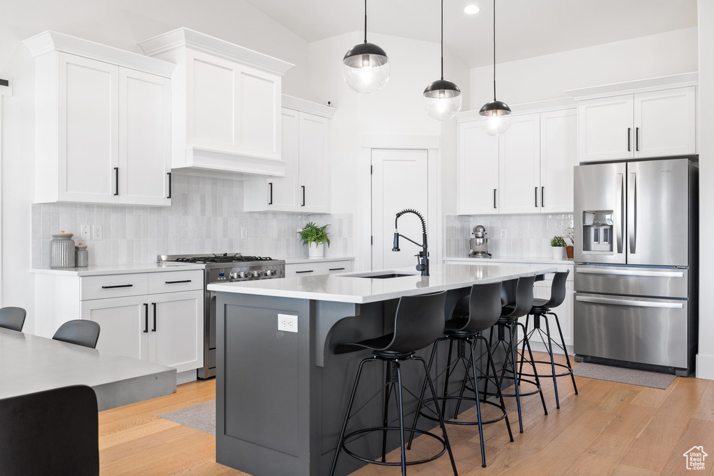 Kitchen with appliances with stainless steel finishes, hanging light fixtures, backsplash, and an island with sink