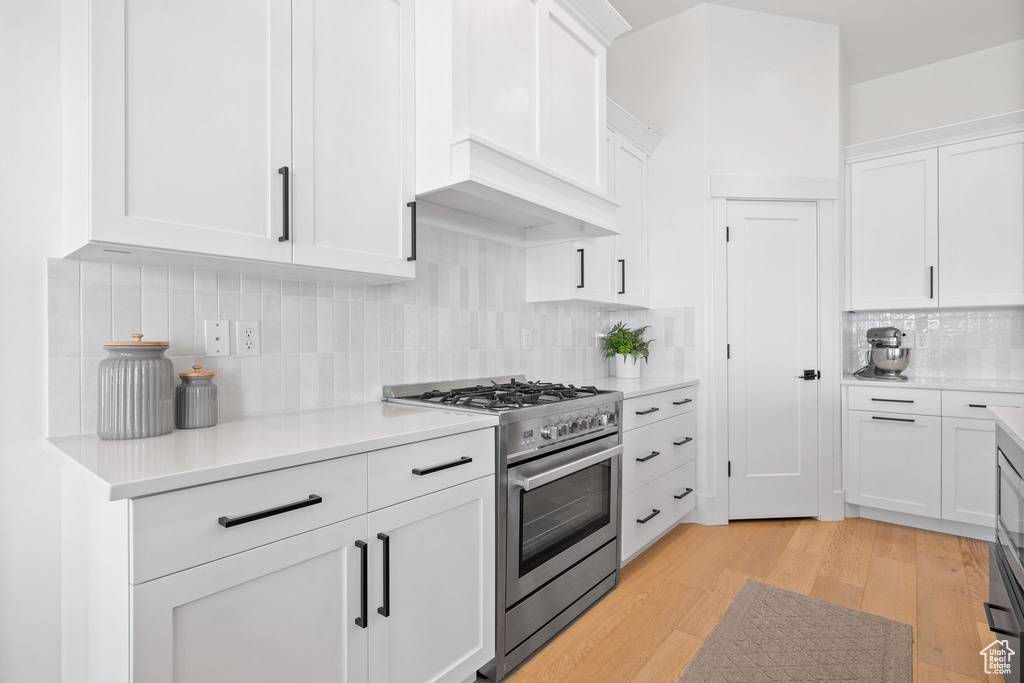 Kitchen with white cabinets, light hardwood / wood-style flooring, tasteful backsplash, and high end range