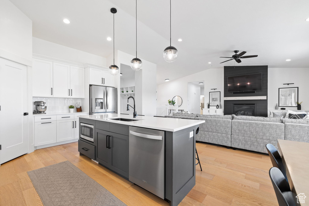 Kitchen featuring a center island with sink, stainless steel appliances, a large fireplace, decorative light fixtures, and white cabinetry