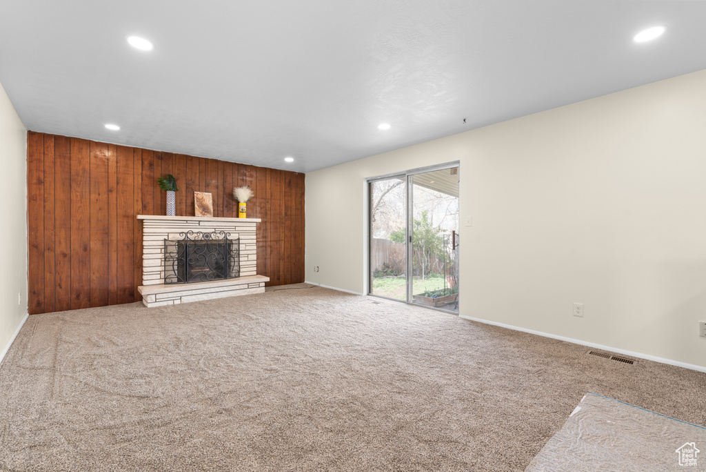Unfurnished living room with carpet, wooden walls, and a stone fireplace