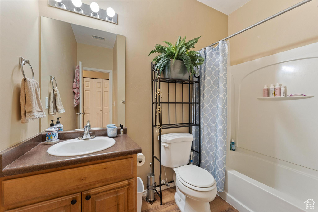 Full bathroom featuring hardwood / wood-style floors, vanity with extensive cabinet space, toilet, and shower / bathtub combination with curtain