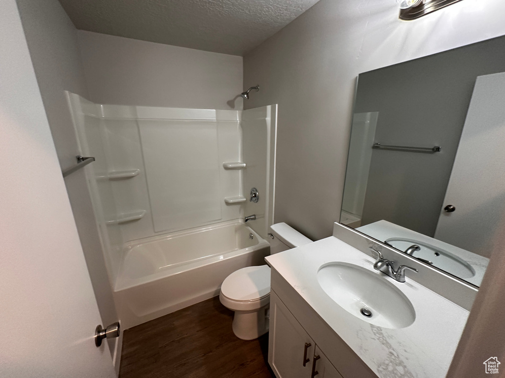 Full bathroom with toilet, vanity, a textured ceiling, washtub / shower combination, and wood-type flooring