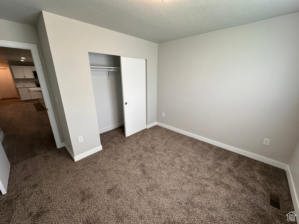 Unfurnished bedroom featuring a textured ceiling, a closet, and dark carpet