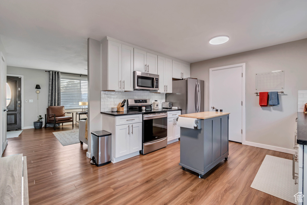 Kitchen featuring light hardwood / wood-style floors, stainless steel appliances, white cabinets, a center island, and tasteful backsplash