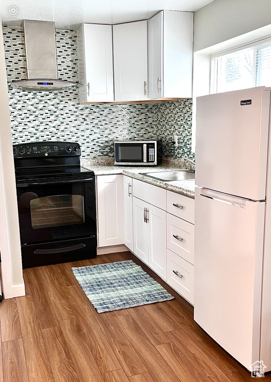 Kitchen featuring white refrigerator, white cabinets, black / electric stove, wall chimney exhaust hood, and tasteful backsplash