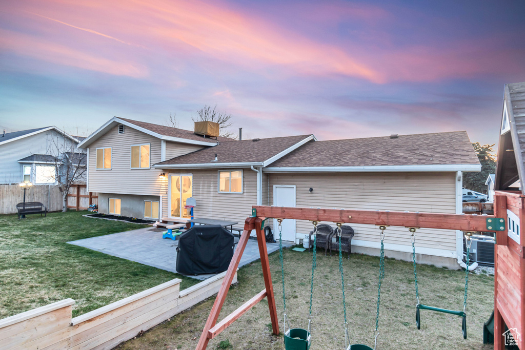 Back house at dusk with a playground, central AC, a patio area, and a yard