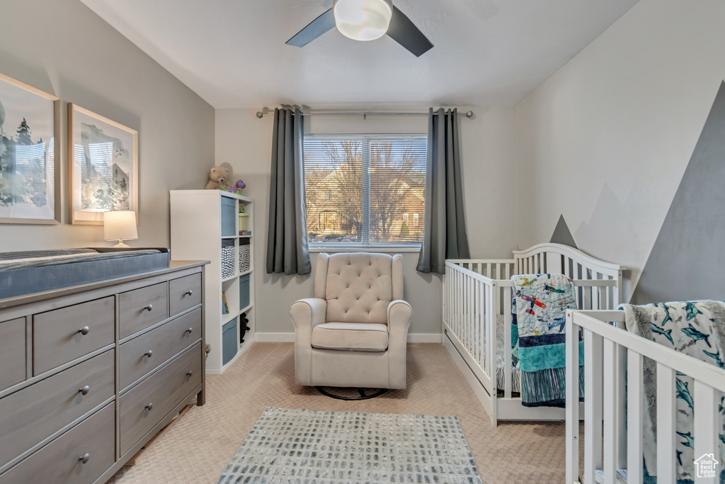 Bedroom featuring light colored carpet, ceiling fan, and a crib