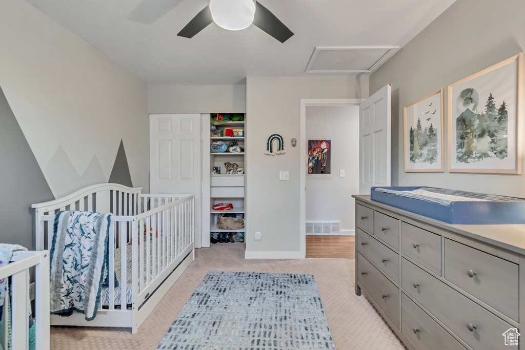 Bedroom with light colored carpet, a crib, and ceiling fan