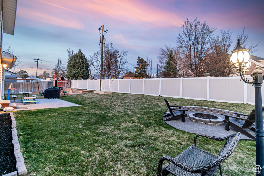 Yard at dusk featuring a playground, an outdoor fire pit, and a patio
