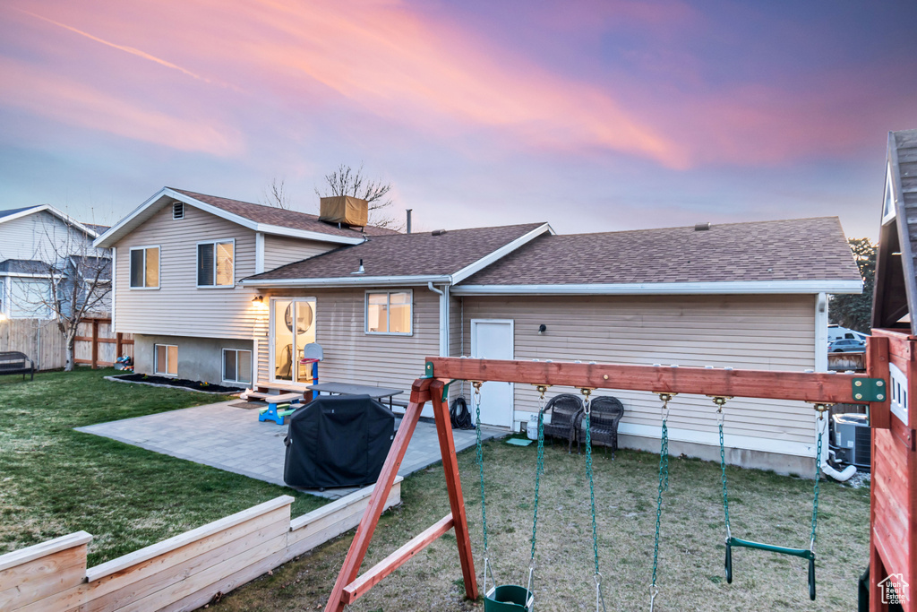 Back house at dusk featuring a yard, a playground, and a patio