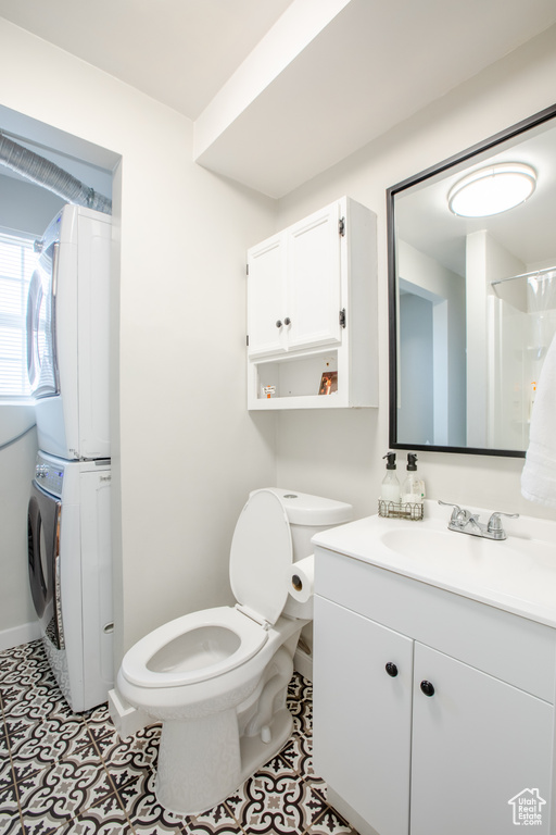 Bathroom with toilet, vanity, stacked washer and dryer, and tile flooring