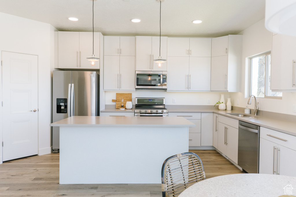 Kitchen featuring white cabinets, hanging light fixtures, stainless steel appliances, and sink