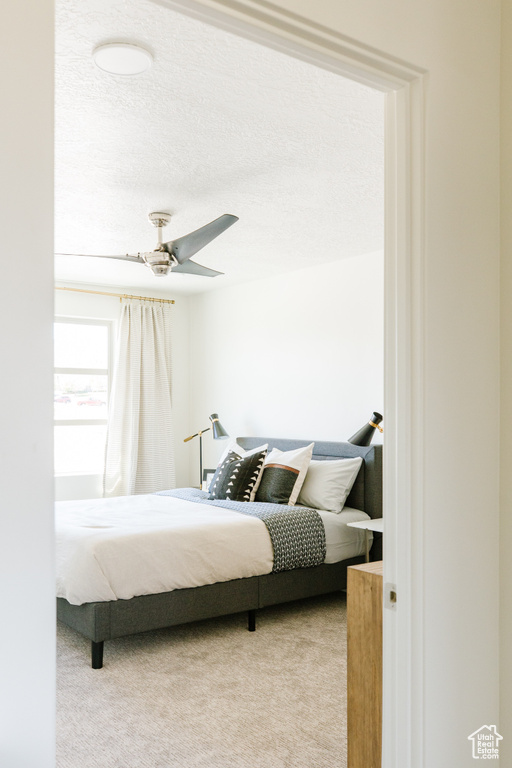 Bedroom featuring a textured ceiling, light colored carpet, and ceiling fan