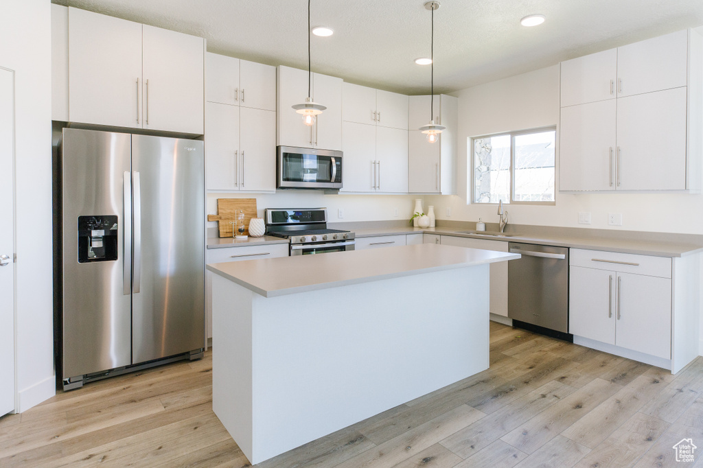 Kitchen featuring light hardwood / wood-style floors, decorative light fixtures, stainless steel appliances, a center island, and white cabinets