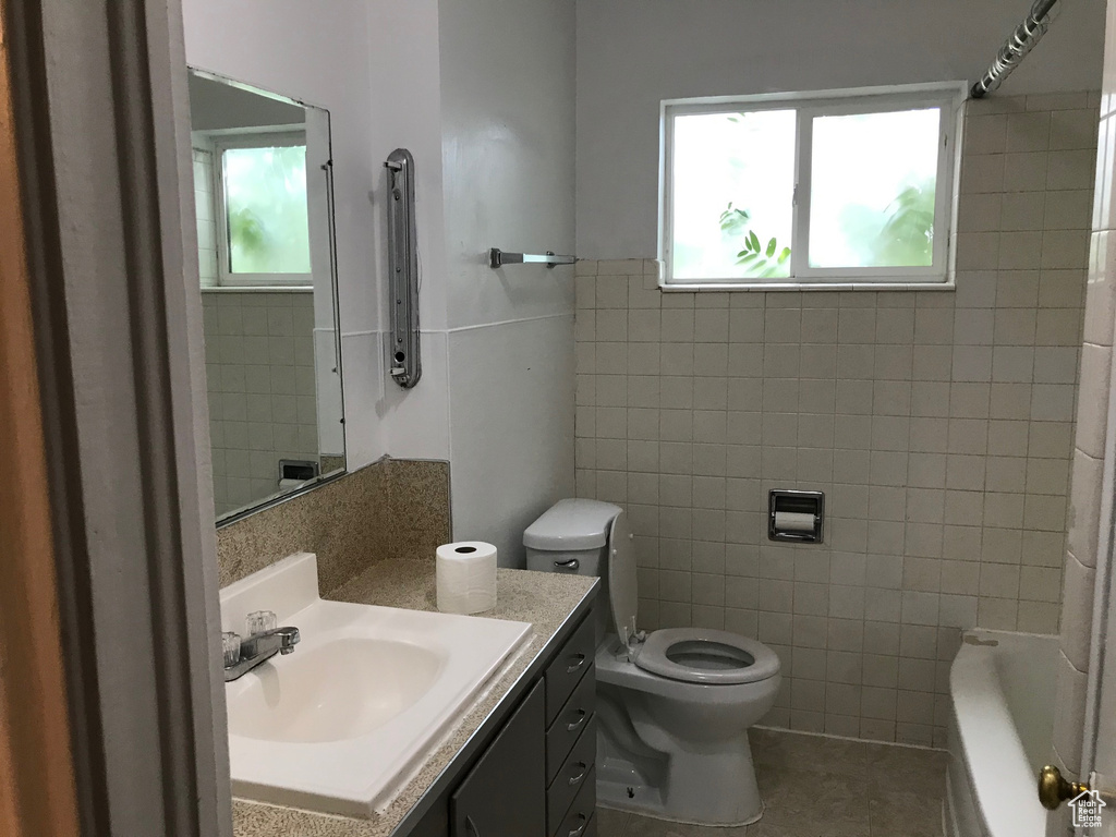 Full bathroom with tile walls, plenty of natural light, vanity, and toilet